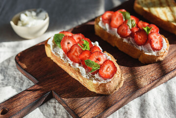 Two toasts or bruschetta with strawberry and cream cheese on wooden board. Summer breakfast. Hard...