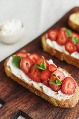 Two toasts or bruschetta with strawberry and cream cheese on wooden board. Summer breakfast