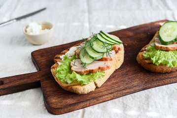 Sandwiches with chicken meat, cucumber, lettuce  and soft cheese on wooden board. Selective focus