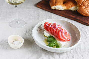 Greek cheese feta with tomatoes, red onion and basil served with wine and fresh baked bread. Selective focus