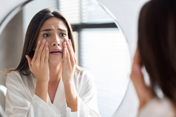Skin Problems Concept. Unhappy Young Woman Looking At Mirror And Touching Face