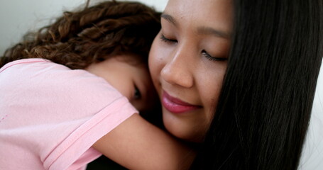 Asian mother cuddling with little daughter in arms, love and affection