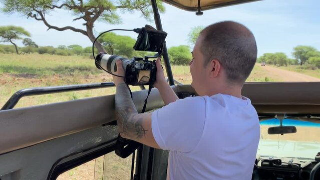 A tourist takes pictures of the amazing nature of Tanzania on a camera with a large lens. Jeep for safari in Tarangire National Park. Safari in Africa.