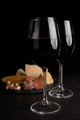 Blurred image on a black background of glasses with red wine and different types of cheeses in the background.