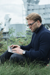 a man works outside in a park on a laptop, remote work and freelance