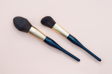 Assortment of female make-up of various face brushes. A set of professional dark blue and golden makeup brushes on a pink background.