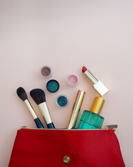 Top view of cosmetics standing out from red cosmetic bag on pink background