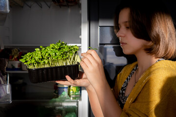 Fototapeta na wymiar a young girl takes out a container with fresh microgreens from the refrigerator, healthy food, eats microgreens