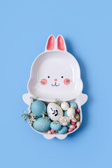 Cute plate in the shape of a bunny with  Easter eggs and candy on blue background. Happy Easter concept.