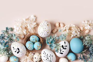 Easter eggs with sweets and flowers on beige. Happy Easter concept. White and blue eggs and cute...