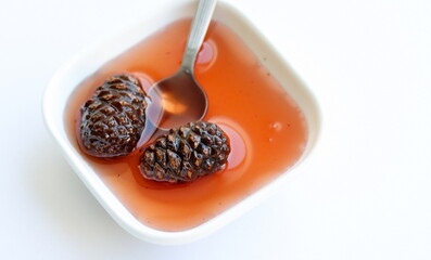 Pine cones jam in bowl, in spoon isolated on white background, on table. Top view.	