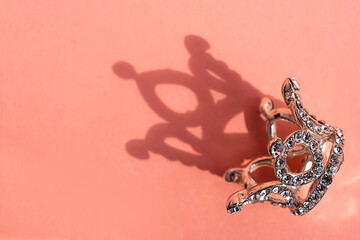 Metal crown with rhinestones on a pink background. With hard shadow. Single object on solid background.