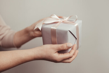 Close up shot of woman hands holding surprise gift package box on pink pastel background with copy...