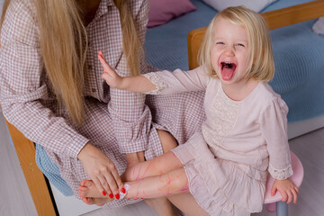 A cheerful child paints her body, a mother wipes her daughter's feet. Preschool Education. Little blonde girl laughing and playing with mom
