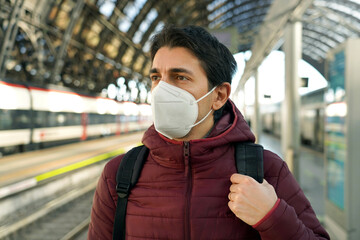 Portrait of traveler man wearing KN95 FFP2 medical face mask with moving train on background on...