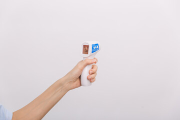 Temperature measurement gun in doctor hands. Close-up shot of doctor wearing protective surgical mask ready to use infrared isometric thermometer gun to check body temperature for virus symptoms.