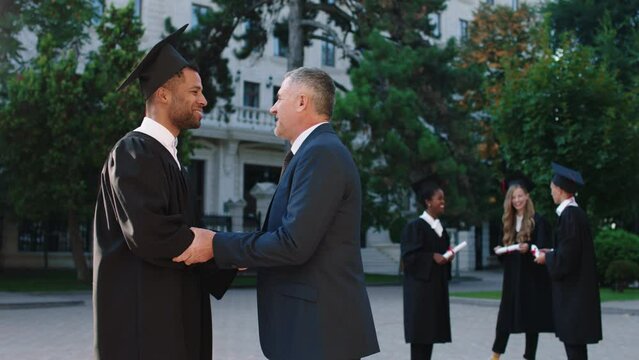 In the college garden graduation day college professor old man congrats his student and giving diploma to him multiracial concept. ARRI Alexa Mini.