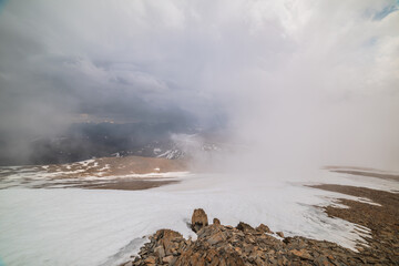 Awesome top view through clouds to high snowy mountains. Scenic landscape with beautiful snow mountains in low clouds. Atmospheric alpine view from stone hill to snow mountain range with low clouds.