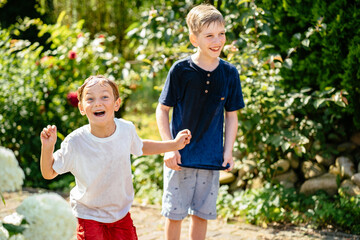 Two cute blond children wet boys exited emotion enjoy sun and playing with garden water hose in...