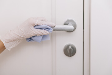 Naklejka premium Cleaning door handle with blue wipe in white gloves. Woman hand using towel for cleaning home room door link. Sanitize surfaces prevention in hospital and public spaces against corona virus.