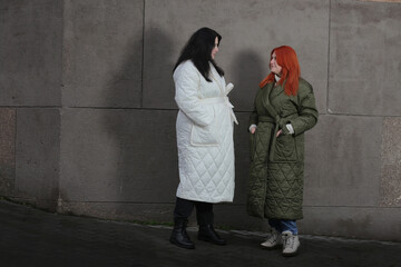 Obraz na płótnie Canvas Two plus-size girls in coats standing against a gray wall.