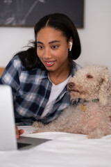 Young woman lying on bed with dog and using laptop
