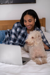 Young woman lying on bed with dog and using laptop