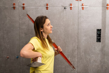 female construction worker holding a level and trowel checking and admiring well done tiling work...