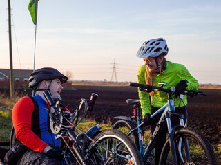 Disabled man on handcycle and woman with bicycle laughing in rural landscape