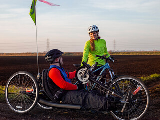 Disabled man on handcycle and woman with bicycle in rural landscape