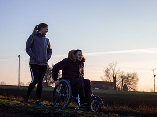 Smiling woman and man on wheelchair in field at sunset