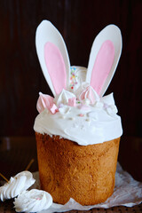 Glazed easter cake decorated with bunny ears cookies, sugar icing and meringues on dark background, copy space. Happy Easter holidays.  Kulich