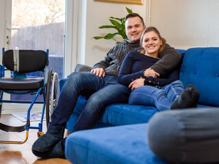 Portrait of smiling couple sitting on sofa next to wheelchair