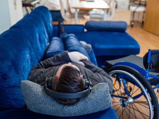 Rear view of man with headphones on sofa next to wheelchair
