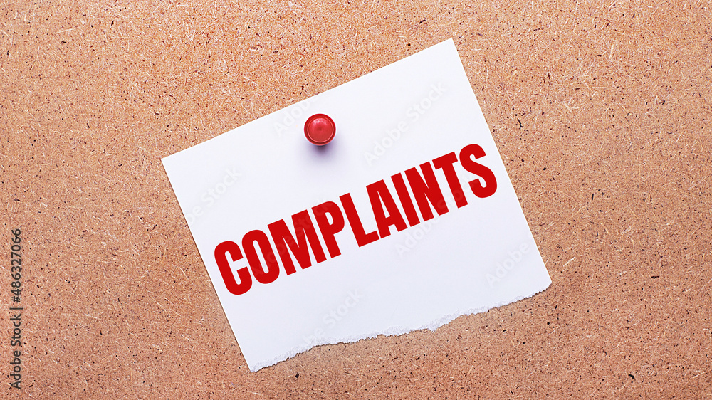 Poster white paper with the text complaints is attached to the wooden background with a red button.