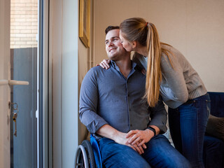 Woman kissing man on wheelchair at home