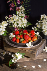 Still life with red ripe strawberries in a ceramic plate with jasmine flowers on an old vintage wooden table