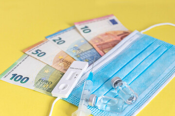 Money (Euro currency banknotes) with medical masks, antigen test, vaccine bottles and syringe. Financial crisis due to Coronavirus losses, selective focus