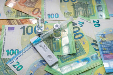 Money (Euro currency banknotes) with medical mask, antigen test, vaccine bottles and syringe. Financial crisis due to Coronavirus losses, selective focus