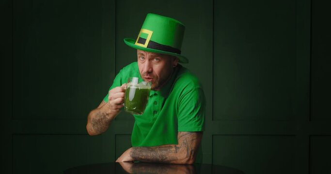 Handsome bearded man drinking green beer on color background. St. Patrick Day celebration