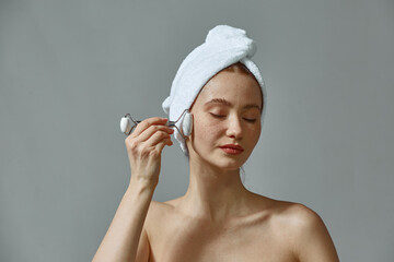 Face lifting massage. Pretty young girl massaging face by jade roller massager, enjoying skincare...