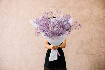 Very nice young woman holding big and beautiful fluffy bouquet of pink gypsophila , cropped photo, bouquet close up on the wooden background