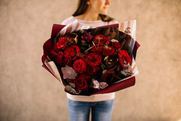Very nice young woman holding big and beautiful bouquet of fresh roses, cymbidium, peony, eucalyptus in burgundy and red colors, cropped photo, bouquet close up on the wooden background - obrazy, fototapety, plakaty