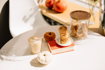 Delicious fresh morning cappuccino coffee standing on an orange book on the white table, decorated with cute little orange pumpkins and cookies, fall style image