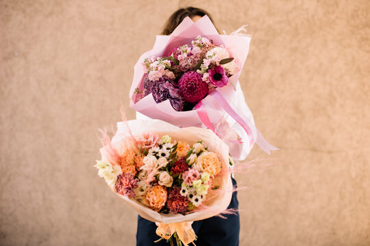 Very nice young woman holding two big and beautiful bouquets of fresh dahlia, chrysanthemum, roses, hydrangea, matthiola, eustoma, pink colors, cropped photo, bouquet close up on the wooden background