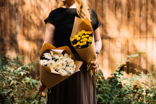 Very nice young woman holding two big and beautiful mono bouquets of fresh chrysanthemum flowers in cream and brown colors, cropped photo, bouquet close up on the wooden background