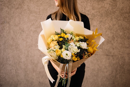 Very nice young woman holding big and beautiful bouquet of fresh roses, eustoma, chrysanthemum, berries, ruskus in white and yellow colors, cropped photo, bouquet close up on the pink background
