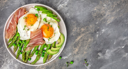 Tasty breakfast. avocado, asparagus, jamon, ham, prosciutto and fried egg on white plate. banner, menu recipe place for text, top view