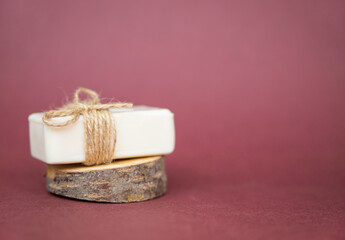 A piece of white soap lies on a cut of a tree on a burgundy background. A natural organic product.