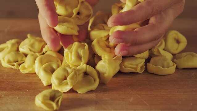 pasta fatta in casa, cucinare cibi freschi. Tortellini della tradizione italiana. Le mani portano in tavola un mazzetto di tortellini. Tipica pasta ripiena per pranzo o cena